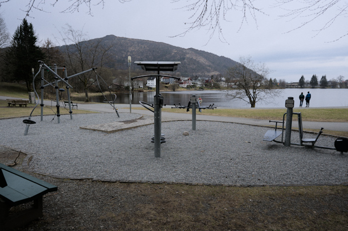 Outdoor gym with various exercise contraptions, located by a lake.